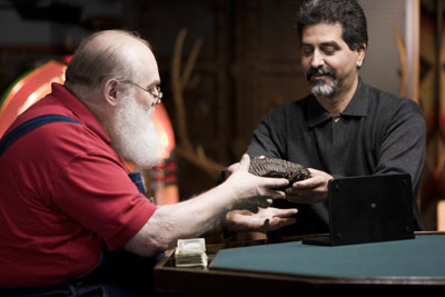 Las Vegas dealer Glen Parshall (left) considers making a cash offer on a fossilized woolly mammoth tooth brought in during the taping of 'Real Deal,' HISTORY Channel's new auction house reality show based at Don Presley Auctions in Orange, Calif. Image courtesy of HISTORY.